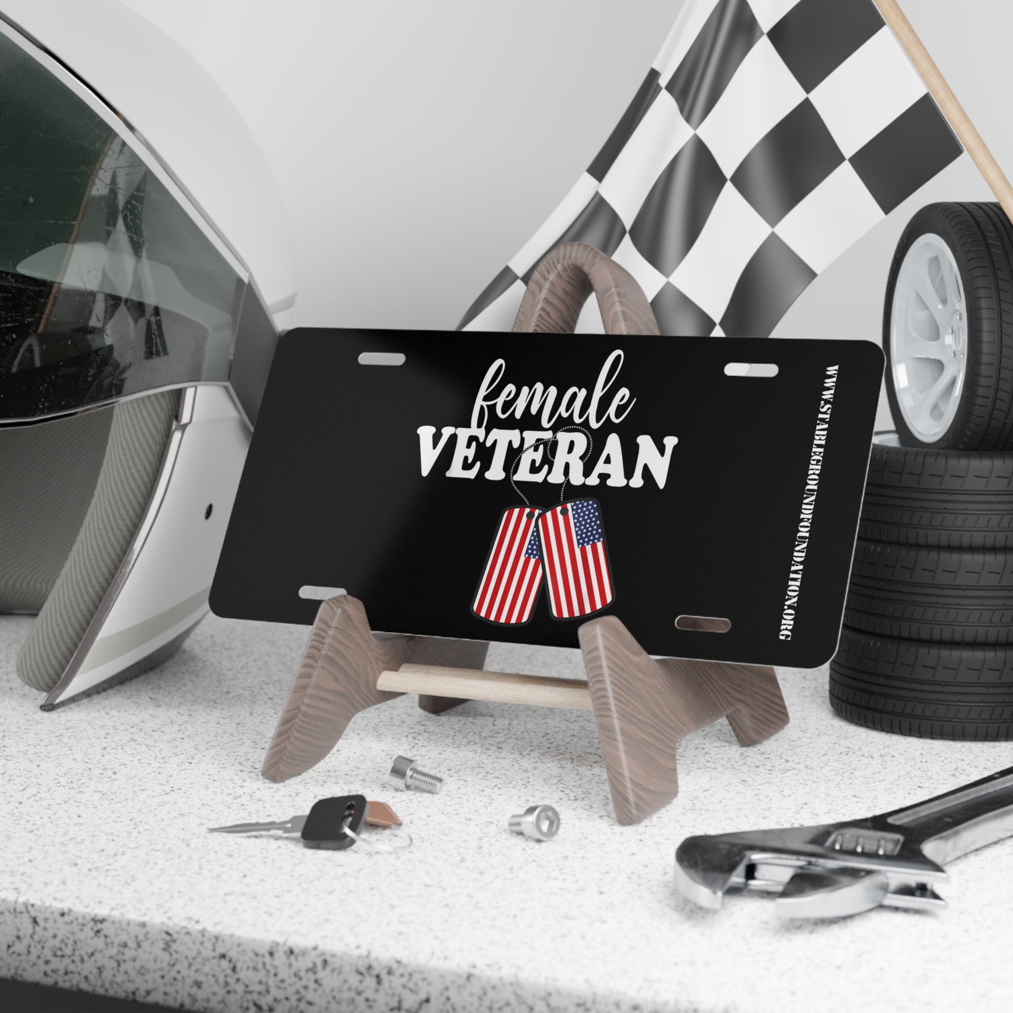Black license plate with bold white text “Female Veteran” and a pair of dog tags featuring the American flag design.