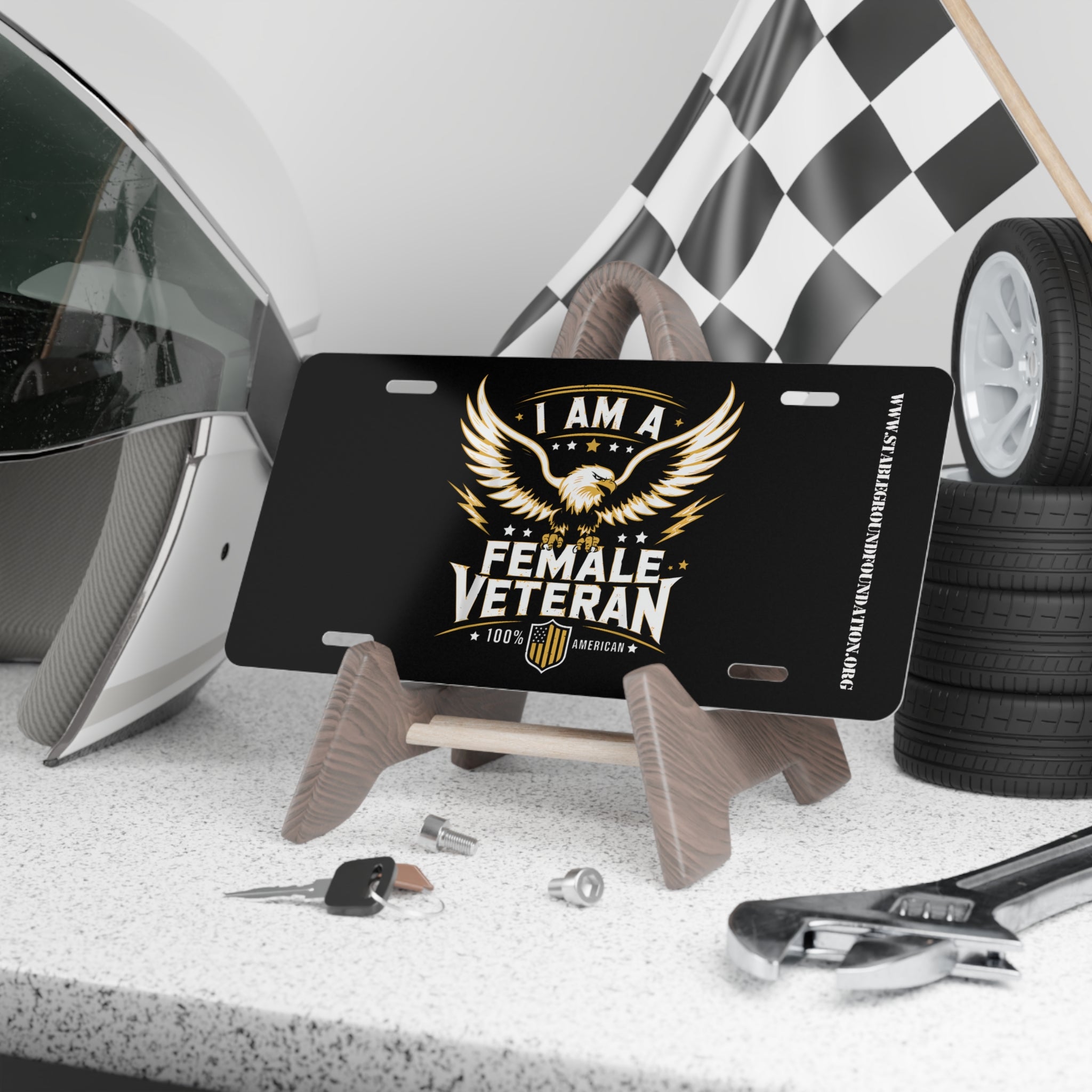 Black license plate with bold white and gold text “I Am a Female Veteran,” featuring a powerful bald eagle with wings spread wide and a patriotic shield emblem.