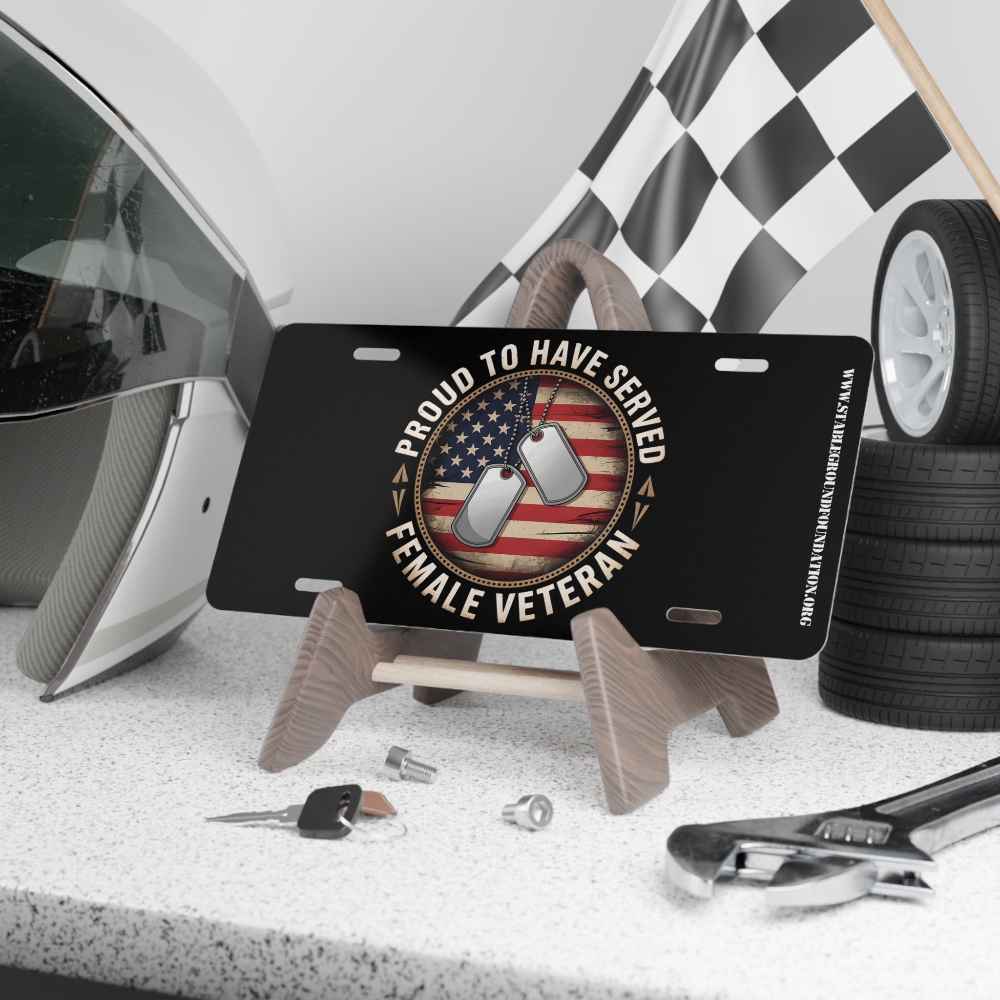 Black license plate with American flag background, dog tags, and text “Proud to Have Served – Female Veteran.”