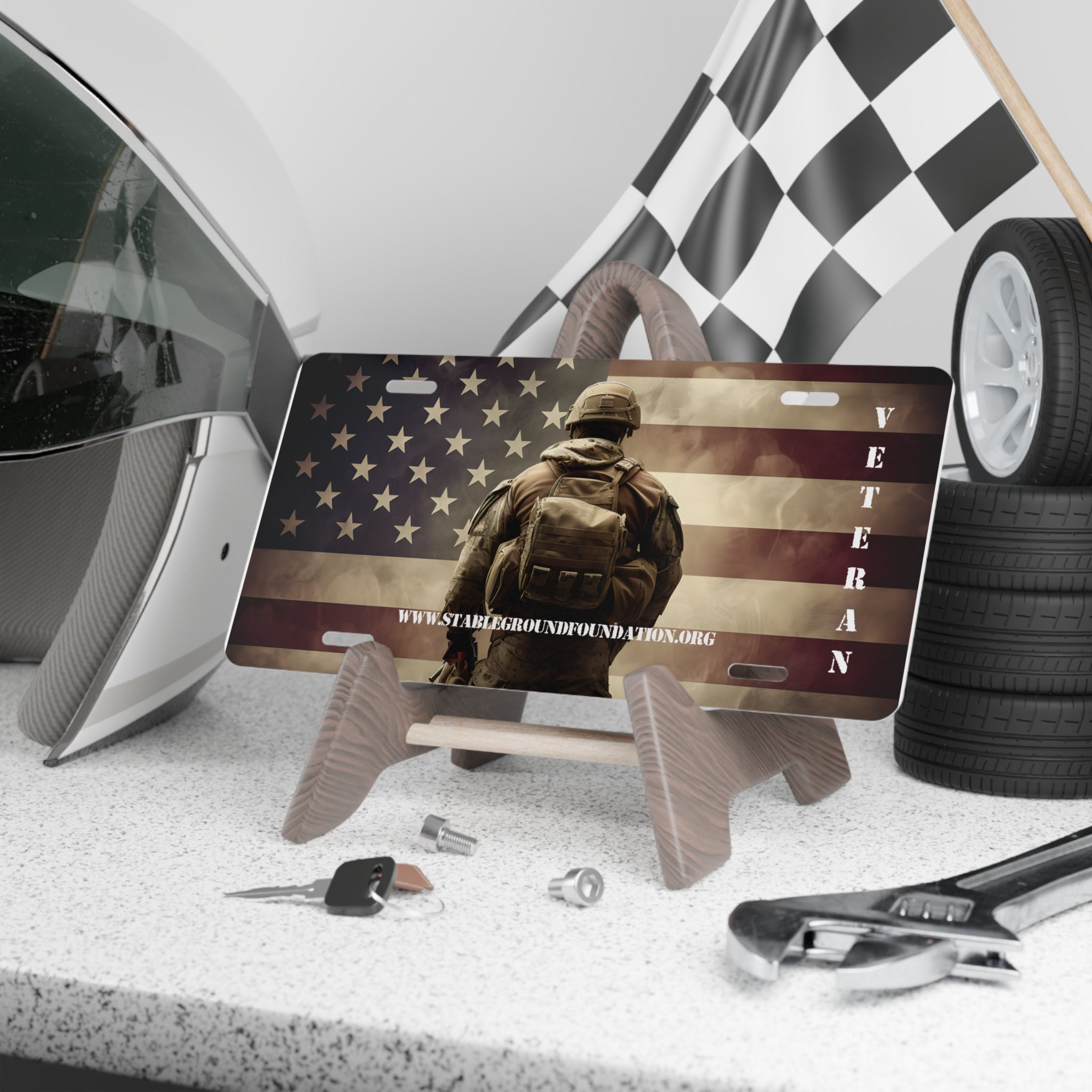 Patriotic veteran license plate featuring soldier silhouette against American flag background with website stablegroundfoundation.org.